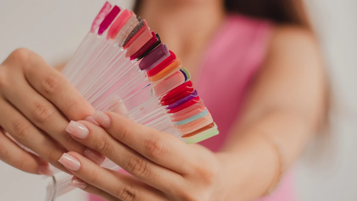 Mãos exibindo unhas delicadas e uma cartela de cores de esmalte